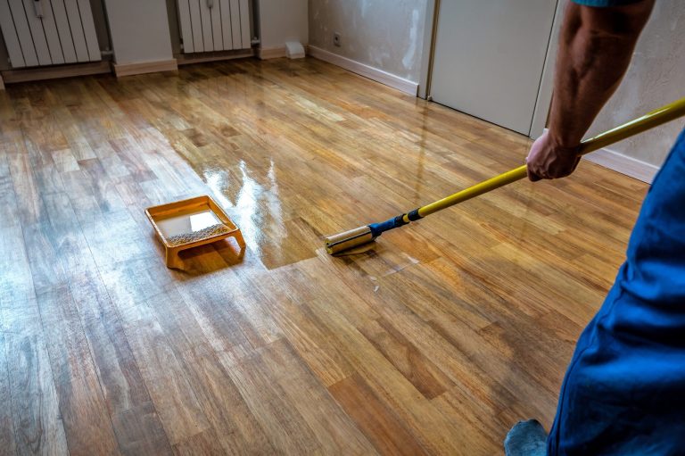 Parquet floor renovation. Lacquering wood floors. Worker uses a roller to coating floor